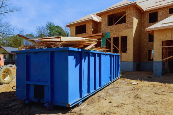 A filled, blue construction dumpster sitting in front of a new home construction project