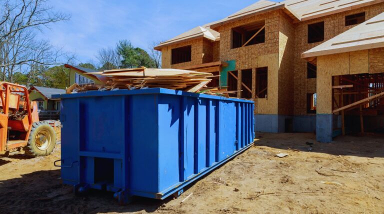 A filled, blue construction dumpster sitting in front of a new home construction project