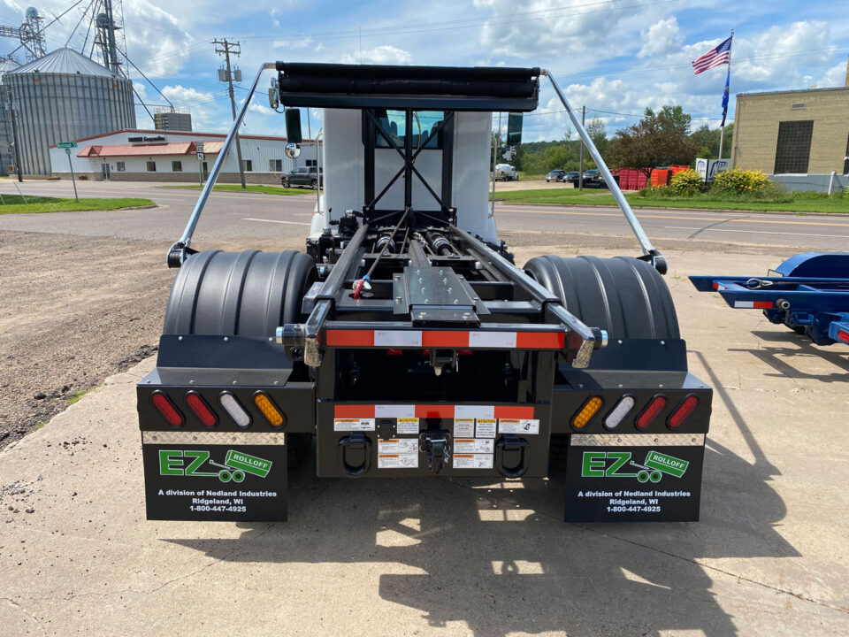 A white roll off truck with an auto tarping system
