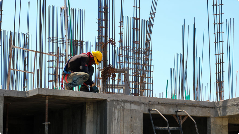 A construction worker crouched on a cement foundation with rebar in the background